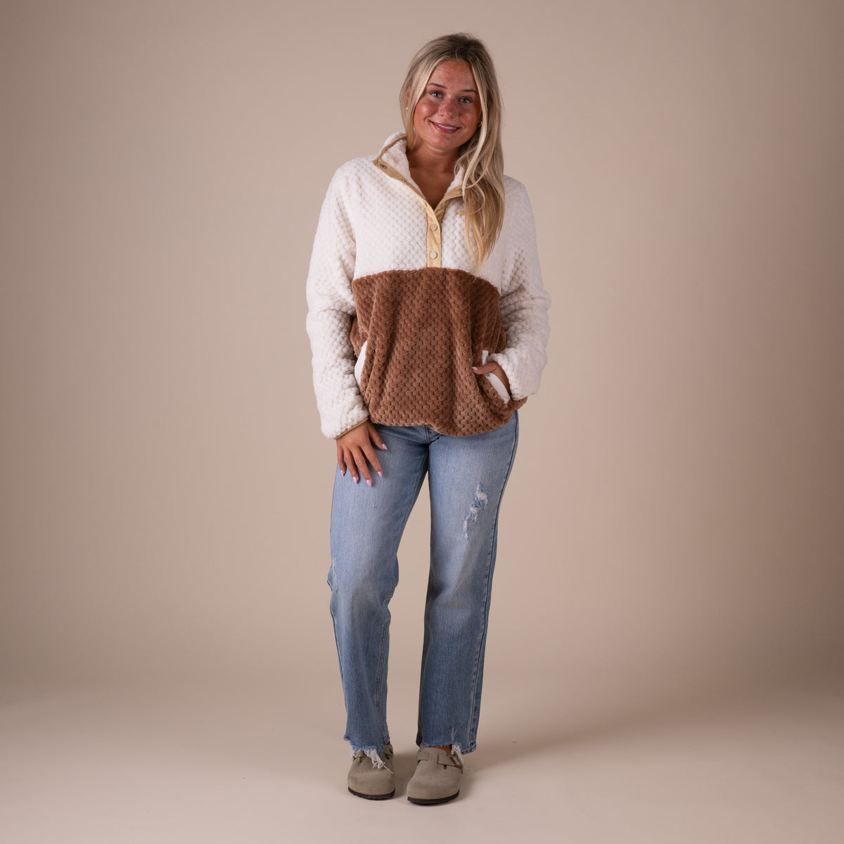Woman wearing a two-tone sweater and jeans on a beige background