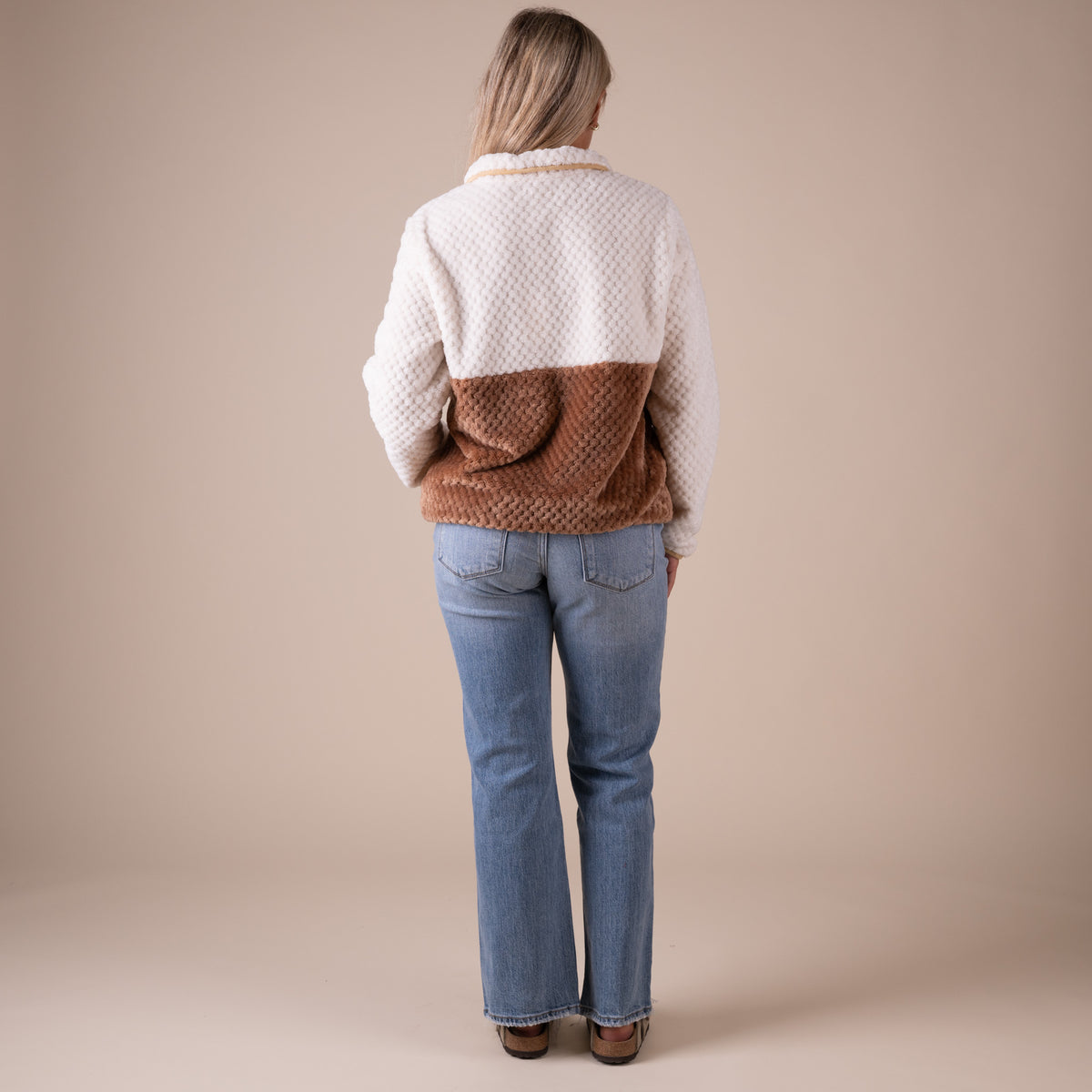 Person wearing a two-tone quilted jacket with white and brown sections on a beige background