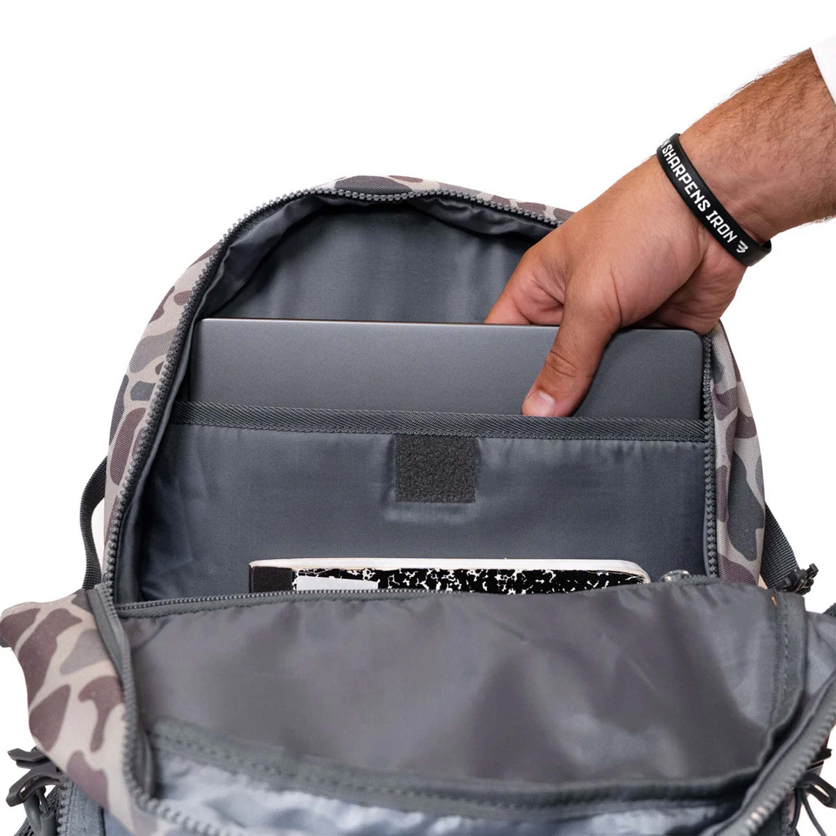 Person placing a laptop into a camouflage backpack with a white background