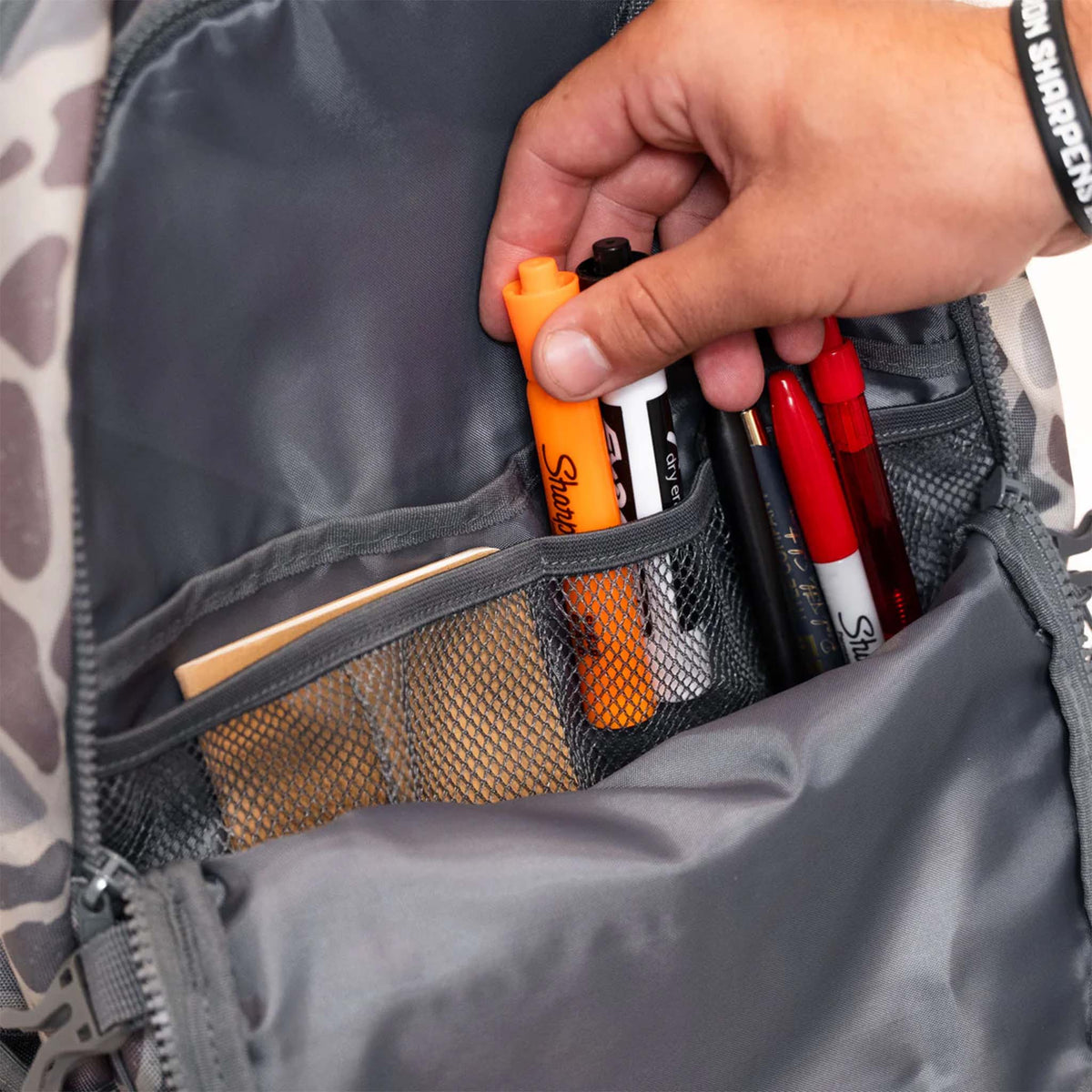 Person reaching into a backpack to grab markers