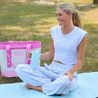 Woman sitting on a yoga mat outside while holding a handled tumbler.