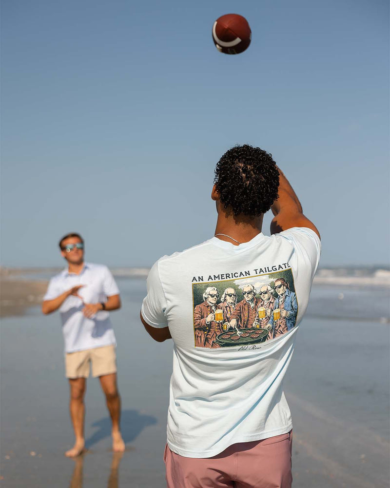 Two guys playing catch with a football on the beach.