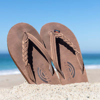 A pair of Rainbow flip flops pushed down in the sand.