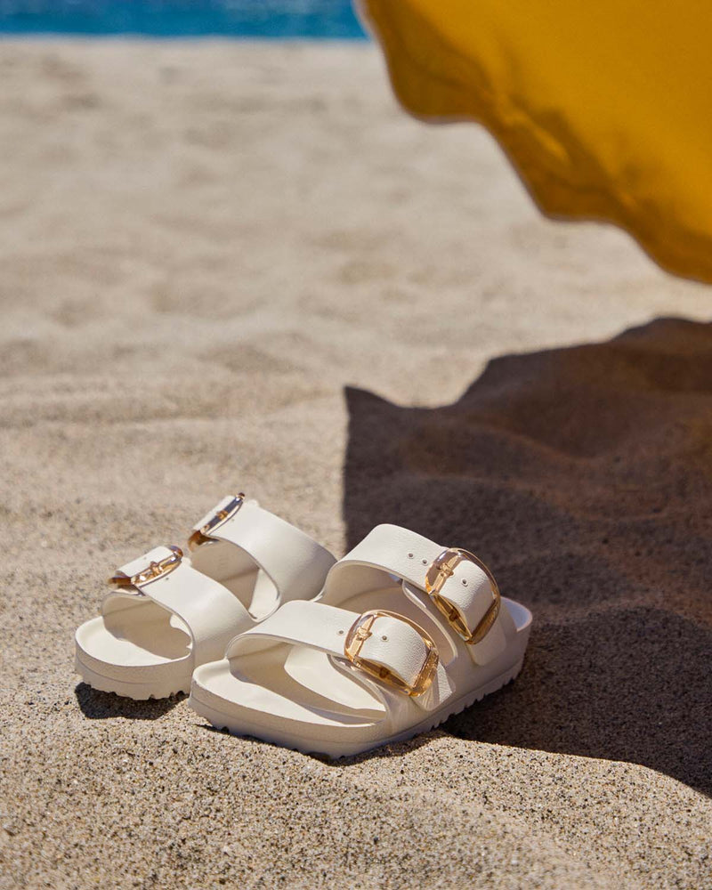 A pair of Birkenstock sandals laying in the sand at the beach.