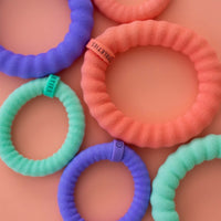 TELETIES colorful ribbed hair ties in coral, mint, and purple displayed on peach background in close-up flat lay.