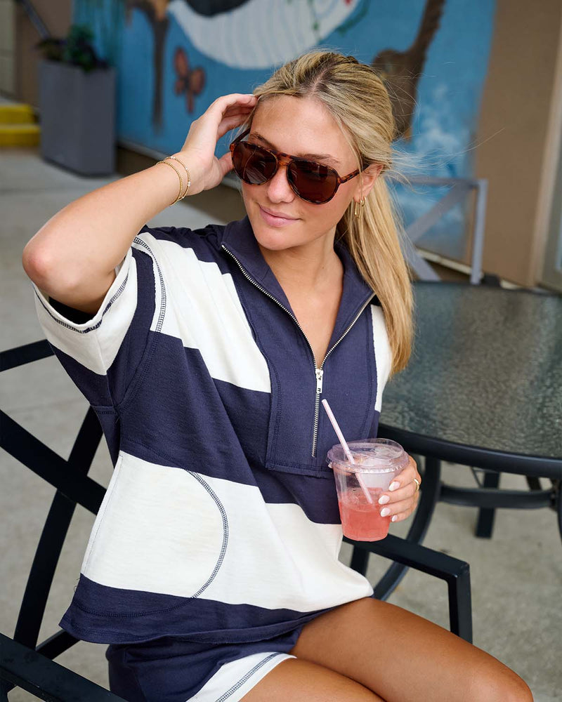 Woman sitting down outside at a table and wearing a blue and white striped FP Movement set.