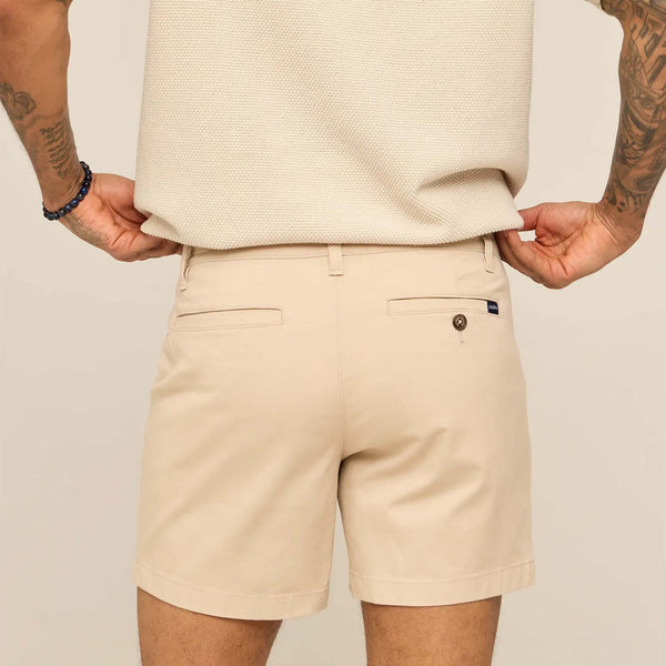 Person wearing beige shorts and a cream sweater on a plain background