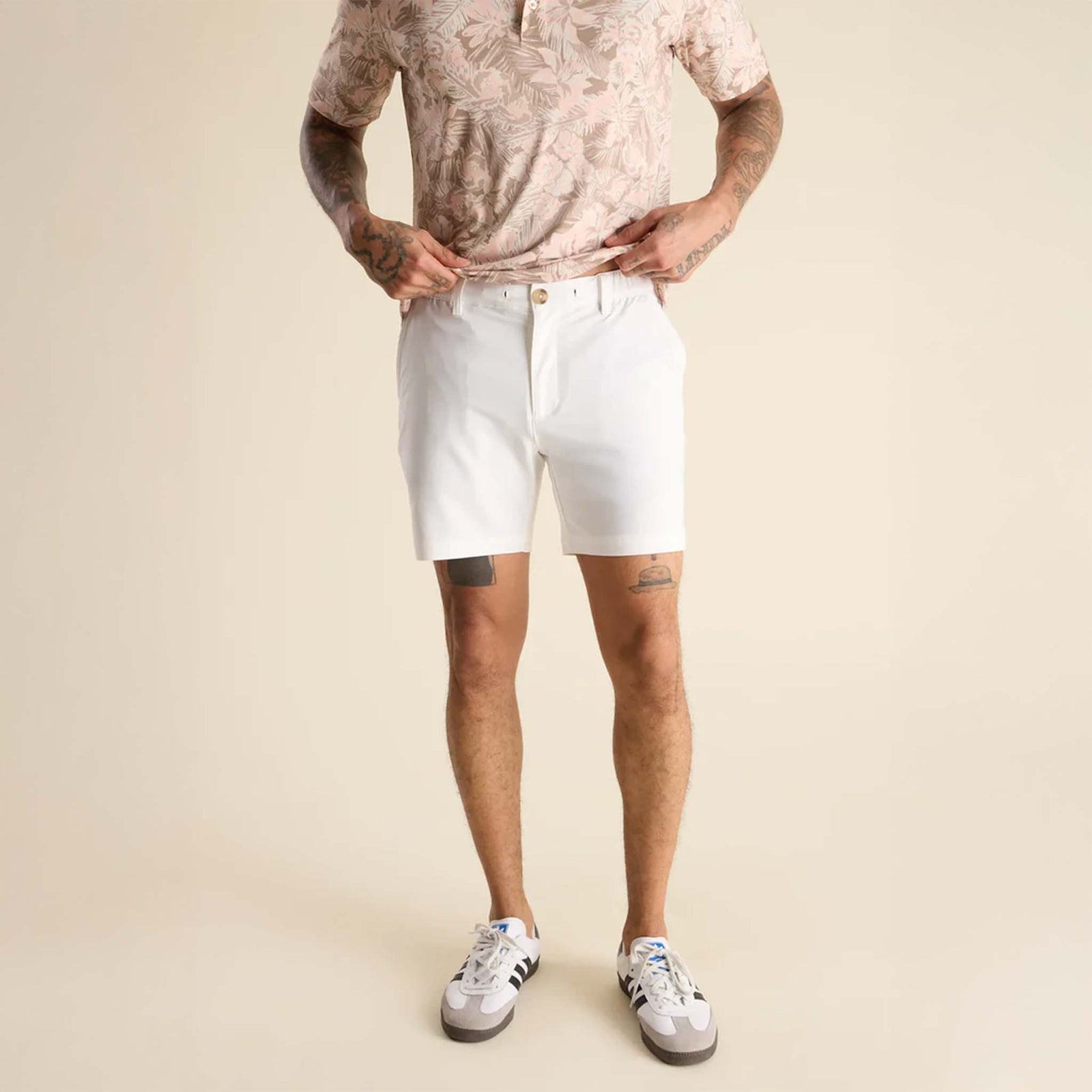 Person wearing a patterned shirt and white shorts on a beige background