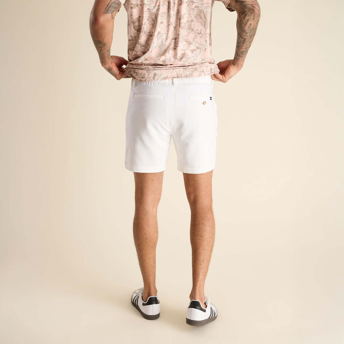 Person wearing a patterned shirt and white shorts on a beige background