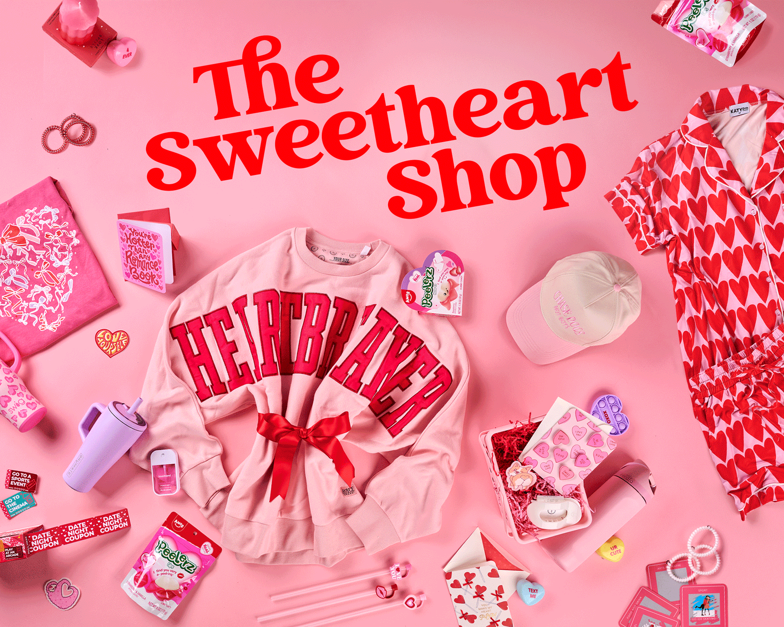 Valentine’s-themed hero banner featuring heart-print pajama sets, pink drinkware, candy, gift items, and a pink crewneck sweatshirt arranged on a blush background with the text “The Sweetheart Shop.”