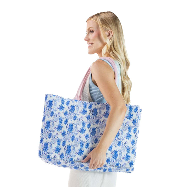 Woman holding a blue floral tote bag on a white background