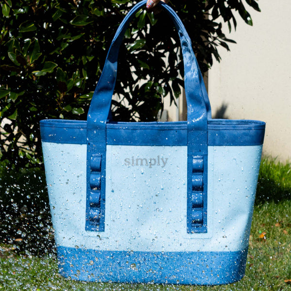Simply Southern Tough Tote in Denim blue shown in an outdoor setting with water splashing to demonstrate the waterproof feature.