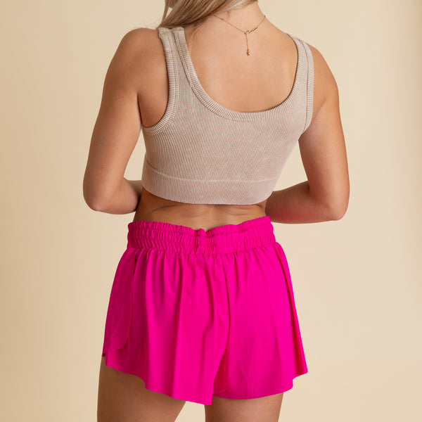  Woman wearing a beige brami tank and bright pink elastic waistband shorts.