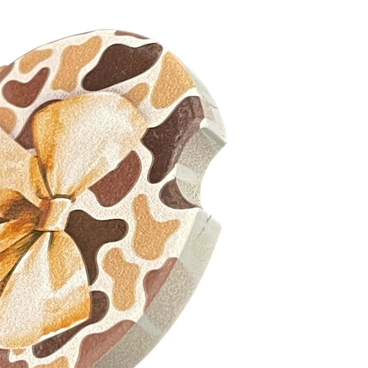 detail shot of car cupholder coaster with brown and beige all over camo print and a large beige bow in the middle.