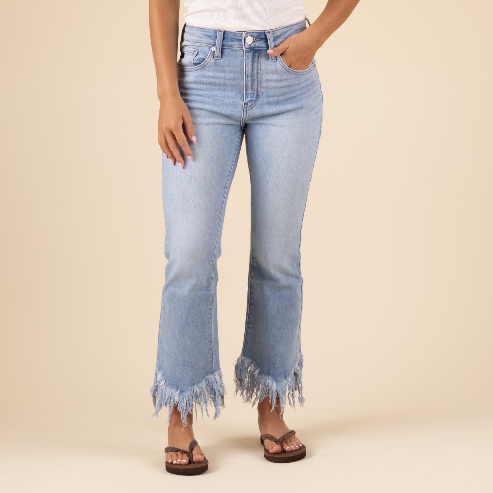 Front view of a woman wearing slightly cropped light-wash jeans with a relaxed fit and frayed hems. The jeans feature subtle fading and whiskering, styled casually with a tucked-in top and shoes, against a neutral background.