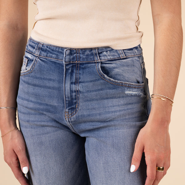 Close-up of the jeans' raw hem and light distressing along the edge, showing the textured denim fabric and slight fade in color.