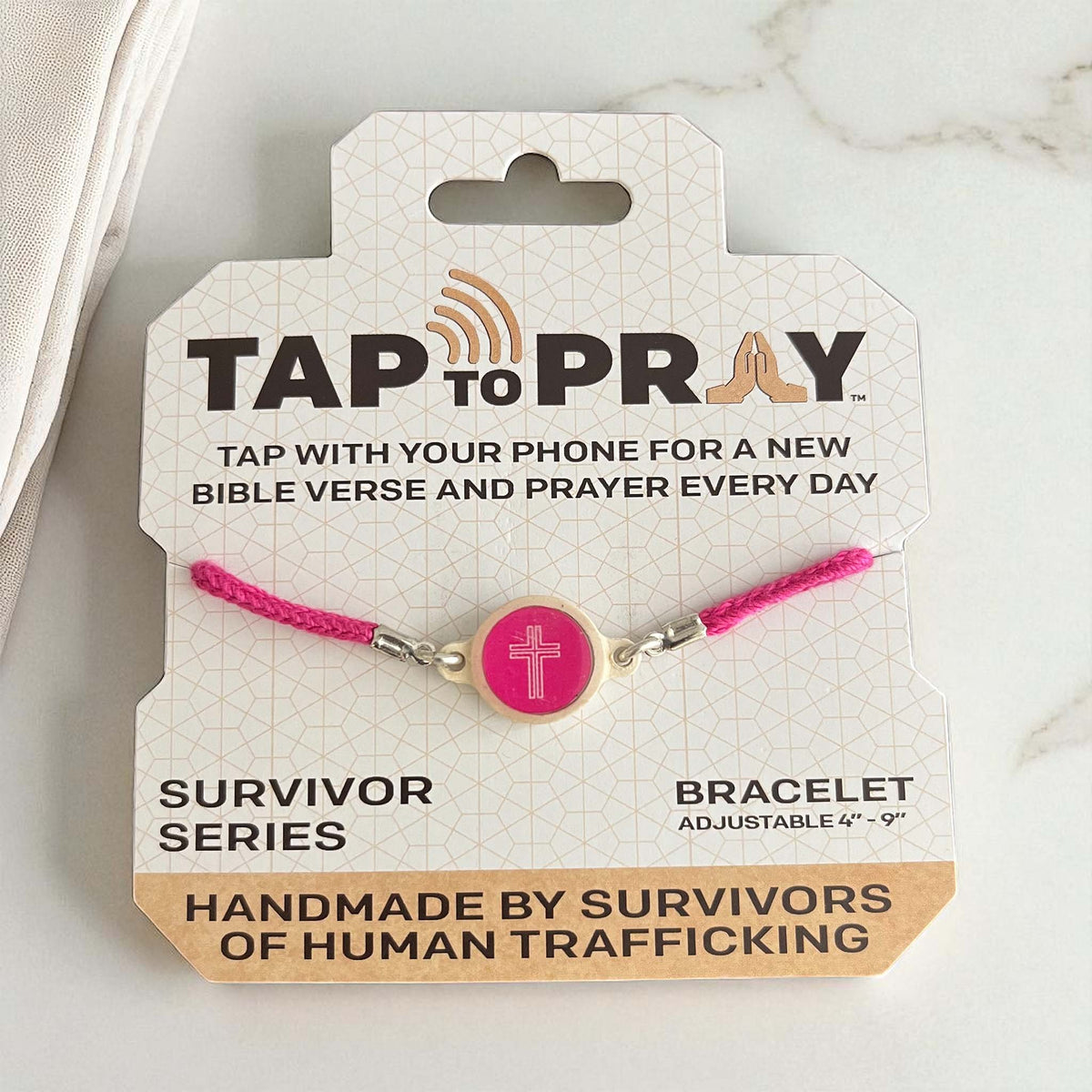 Tap to Pray Survivor Series bracelet with pink braided cord and round pink charm featuring a white cross, displayed on branded card.