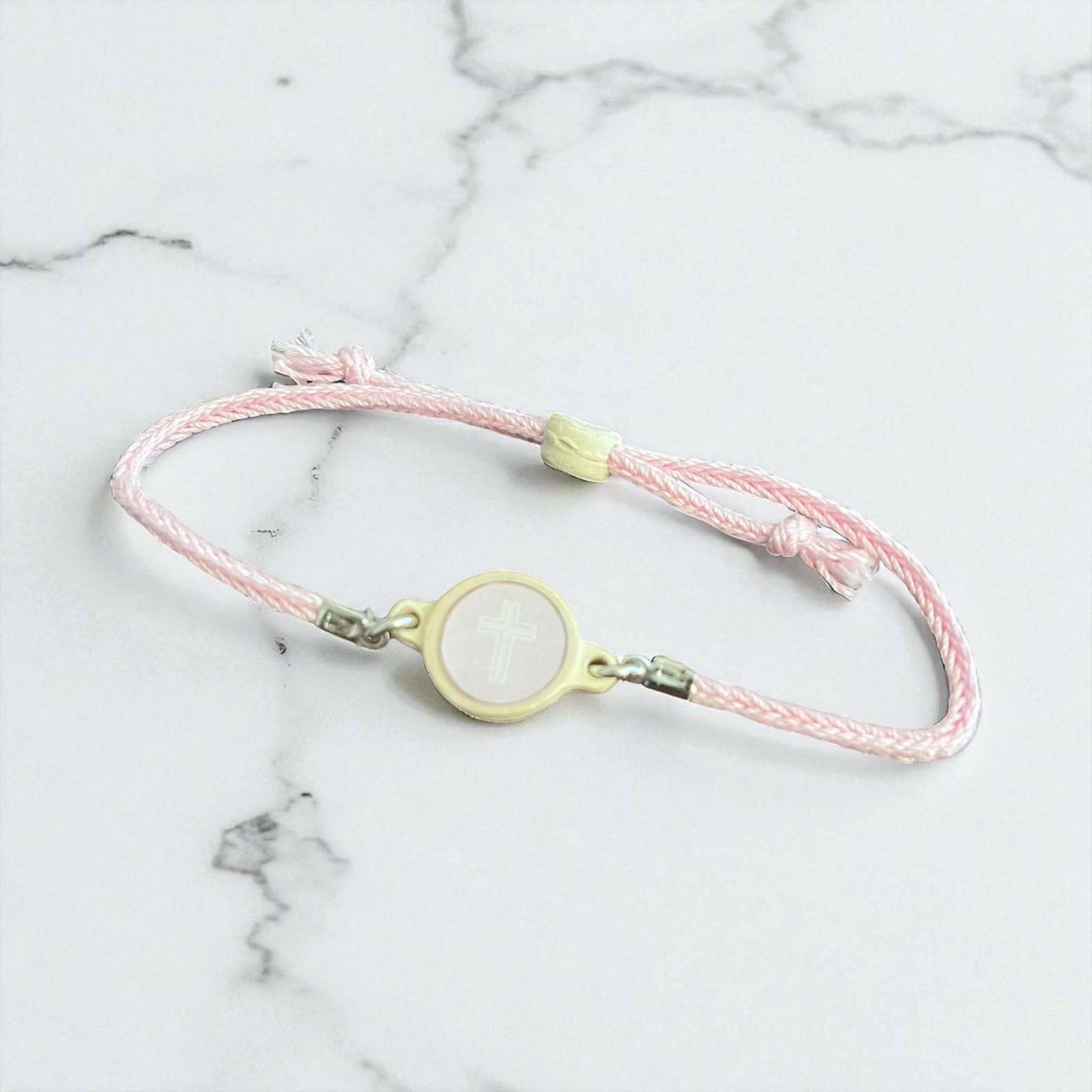 Pink braided bracelet with a yellow clasp on a marble surface