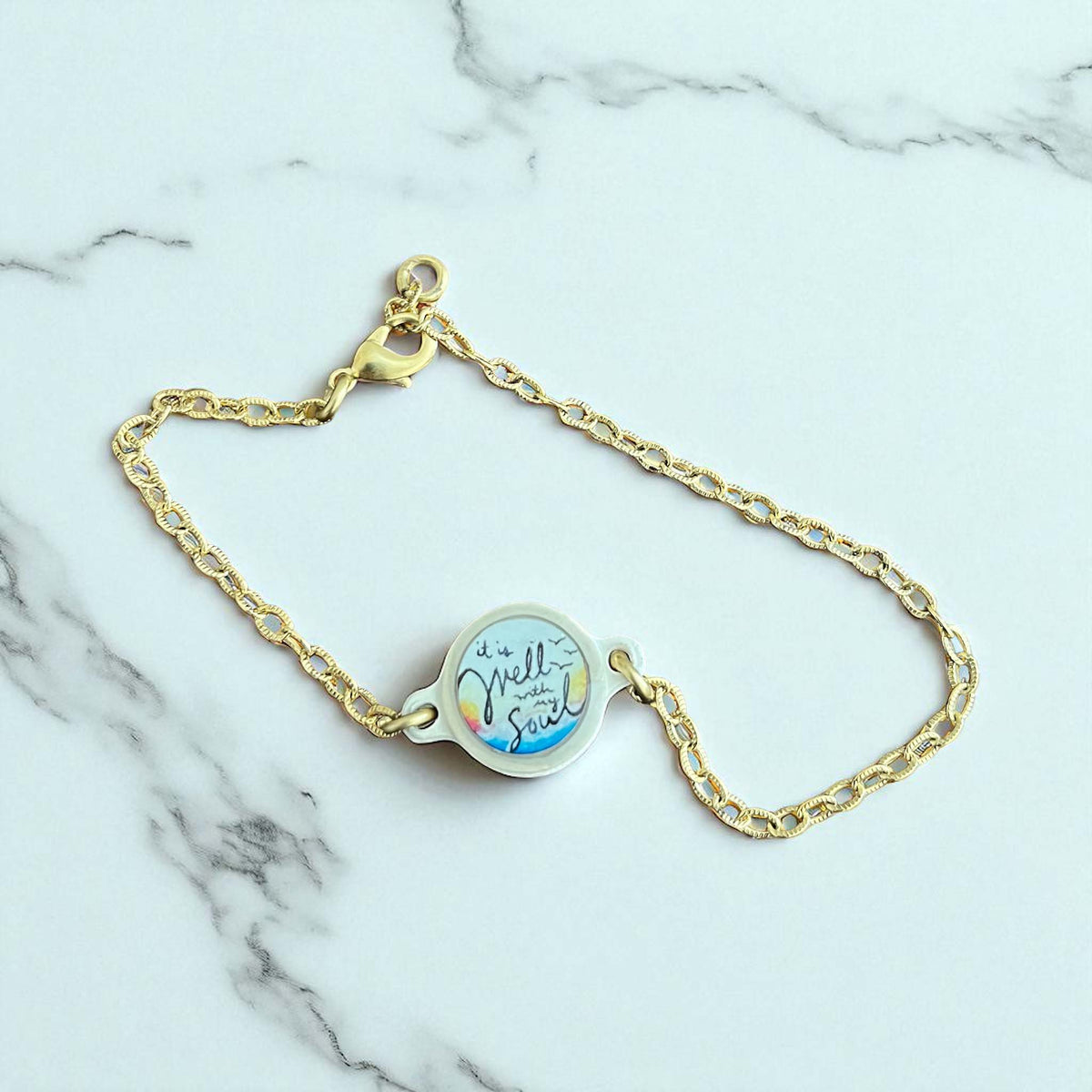 Gold bracelet with a blue and white charm on a marble background