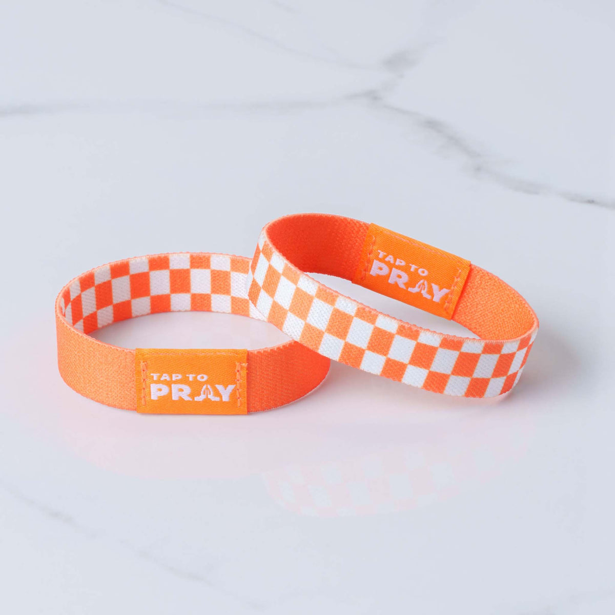 two stacked Tap To Pray Wristband in Orange and White checkered pattern on one side, solid orange on reverse side.