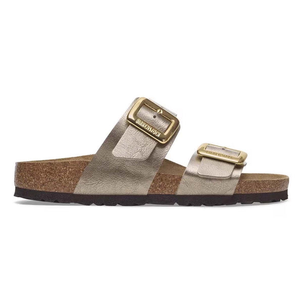 Birkenstock Sydney Luxe Buckle Sandals in Taupe, sizes 5/36, 6/37, 7/38, 8/39, 9/40, 10/41, 11/42. Profile shot of a sandal showing dual metallic taupe straps with gold buckles and cork sole against a white background.