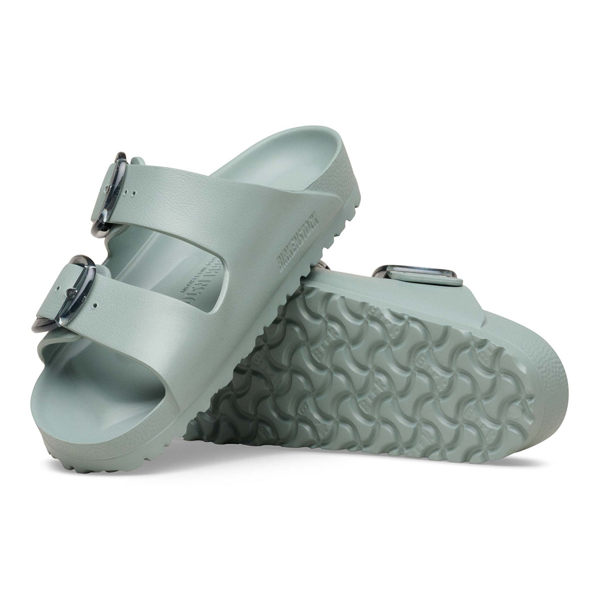 Birkenstock Arizona EVA sandals in Pure Sage with two adjustable straps and translucent buckles, shown with one sandal upright and the other displaying the textured outsole tread.