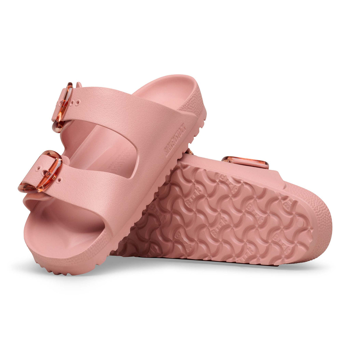Birkenstock Arizona EVA sandals in Pink Clay with two adjustable straps and translucent oversized buckles, shown with one sandal upright and the other displaying the textured outsole tread.