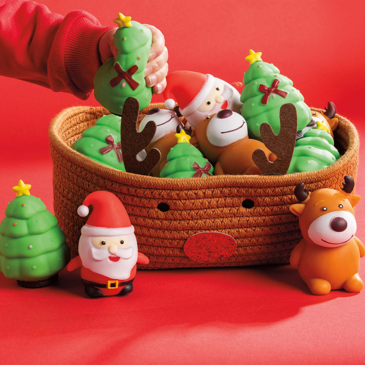 Basket of Christmas squeeze toys with Santa, reindeer, and Christmas tree designs, displayed on a red background.