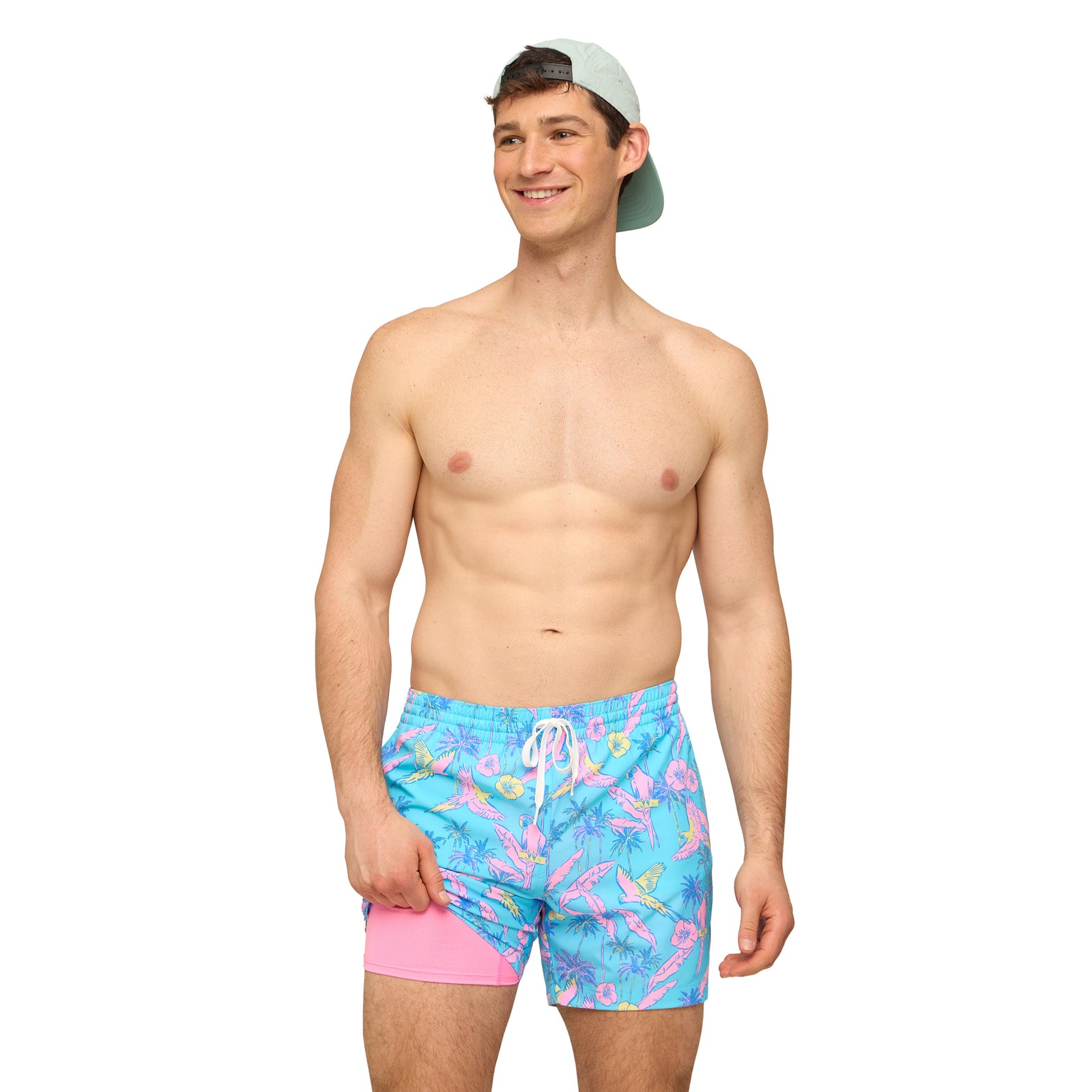 Man wearing turquoise blue swim shorts with all over pink and yellow bird pattern in front of a white background.