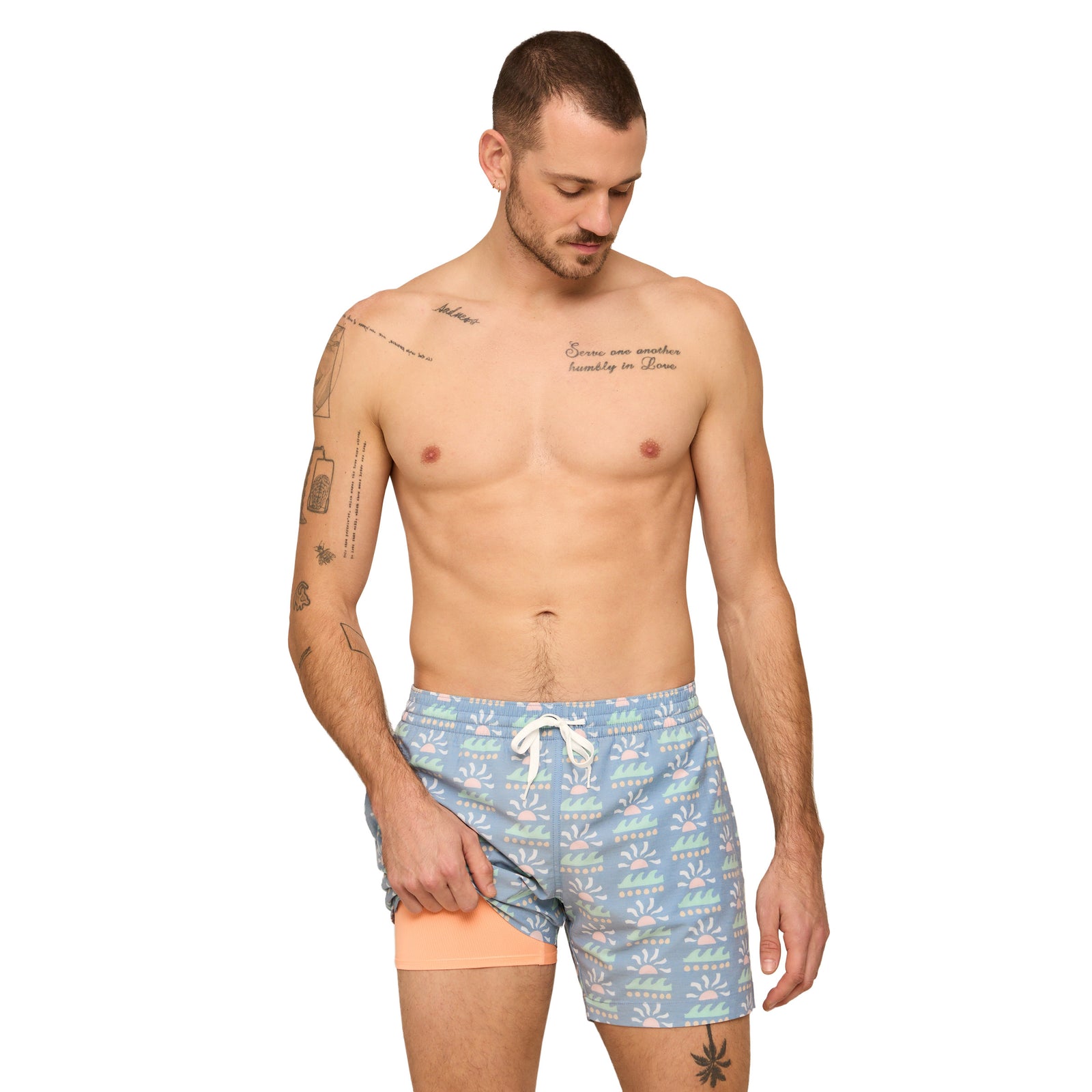 Man wearing blue swim shorts with a sunset ocean all-over pattern on a white background.