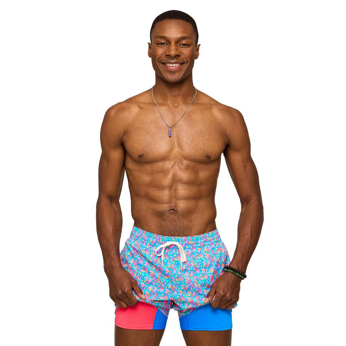 Man wearing colorful swim shorts holding fabric up on legs to show shorts liners standing in front of a white background