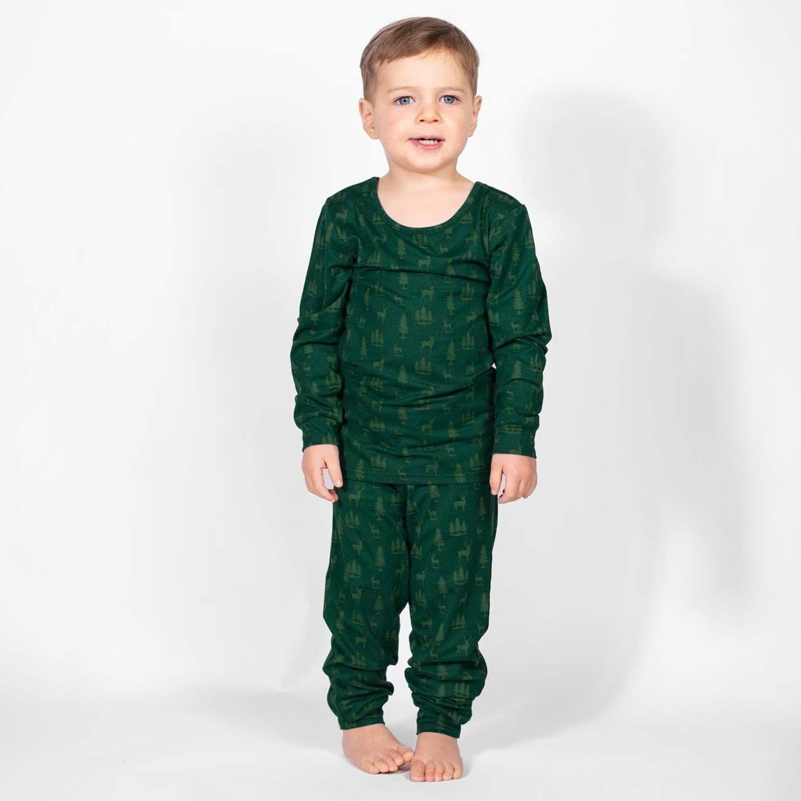 Toddler wearing green woodland pajama set with long-sleeve top and pants featuring deer and tree print.