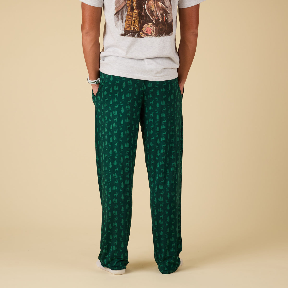 Person wearing green patterned pants and a white t-shirt on a beige background