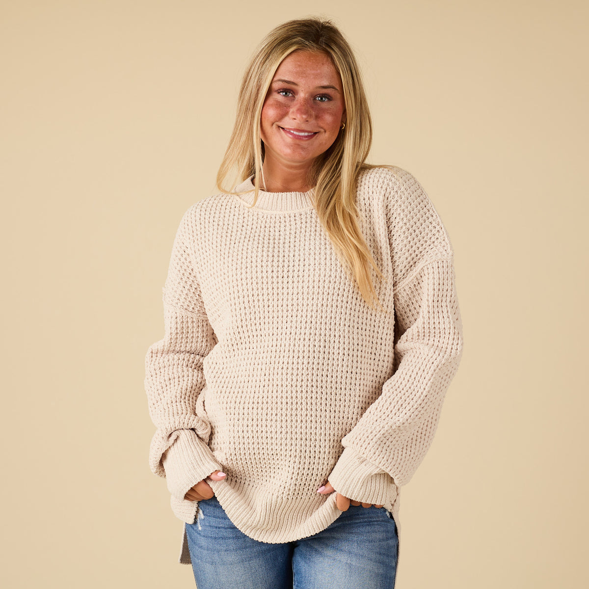 Woman wearing a beige sweater and blue jeans against a beige background