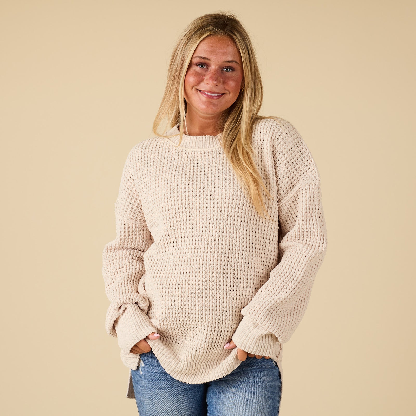 Woman wearing a beige sweater and blue jeans against a beige background
