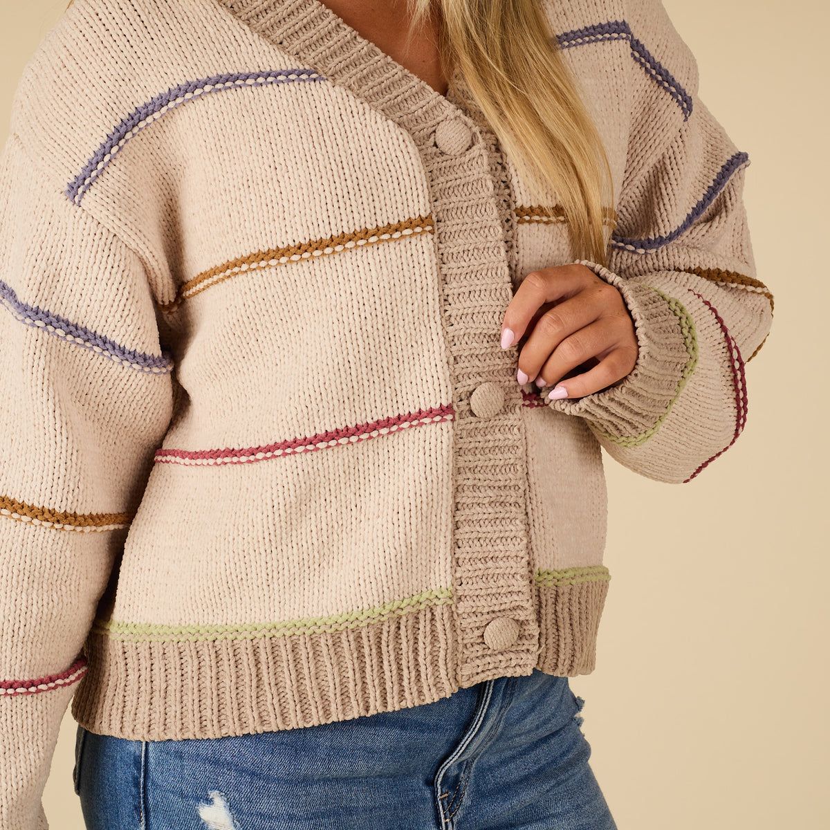 Beige cardigan with colorful trim worn by a person on a beige background