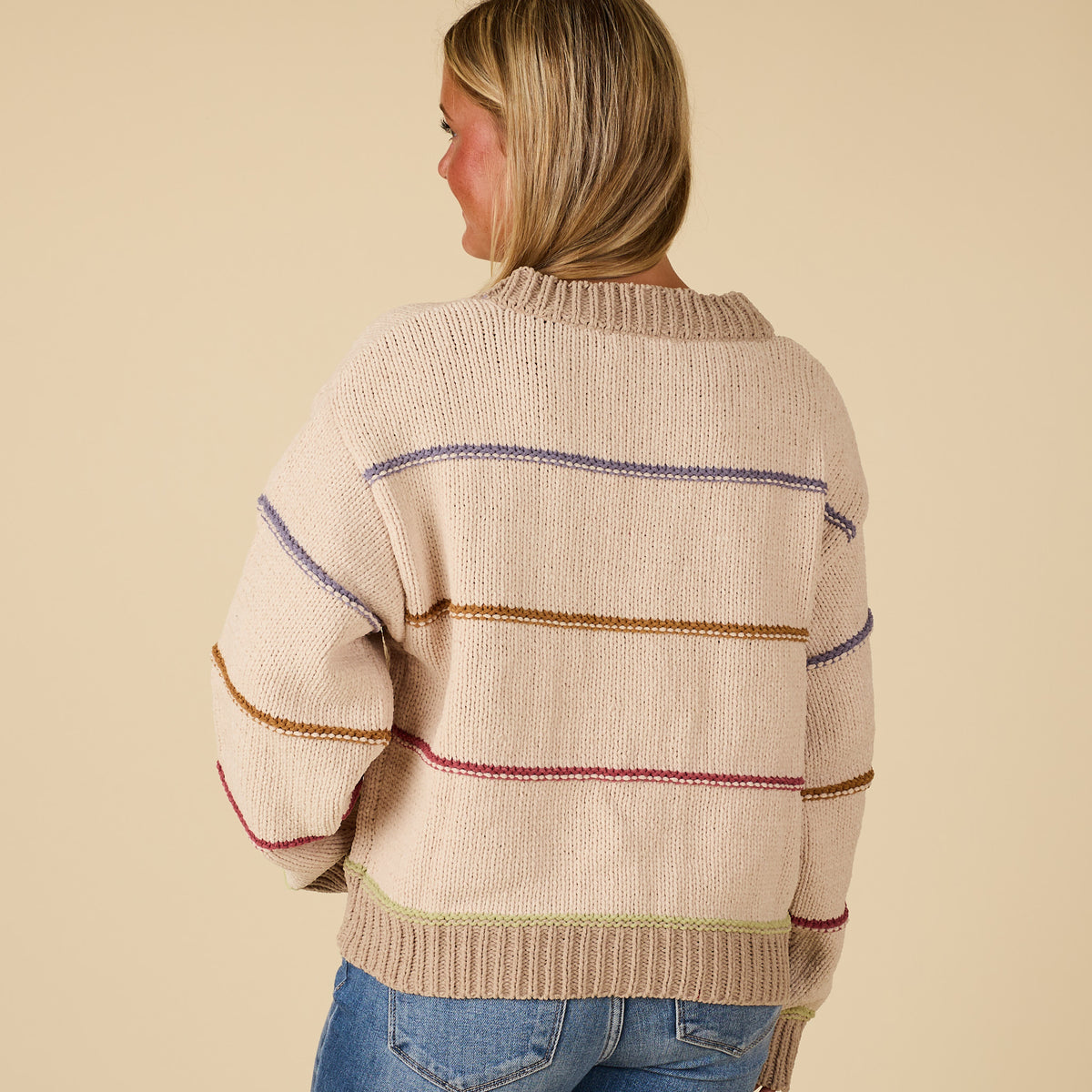 Woman wearing a beige sweater with colorful stripes on a beige background