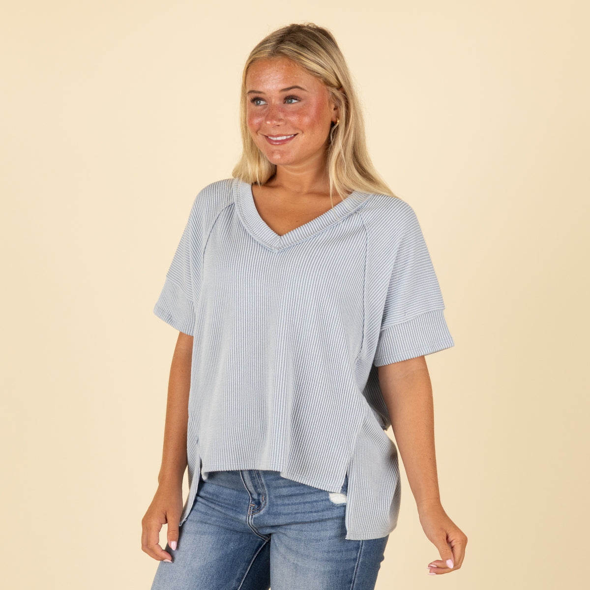 Woman wearing a light blue top and jeans on a beige background