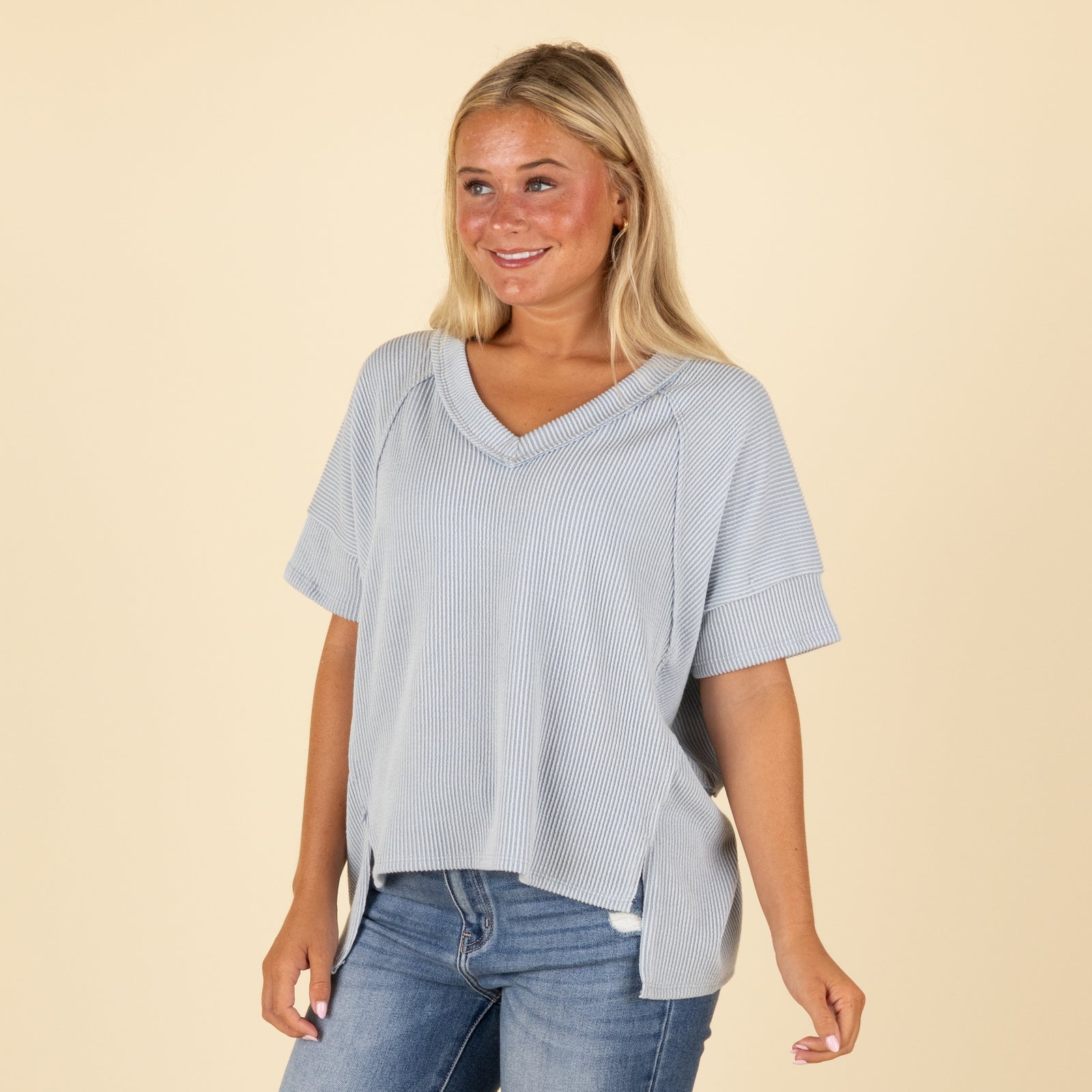 Woman wearing a light blue top and jeans on a beige background