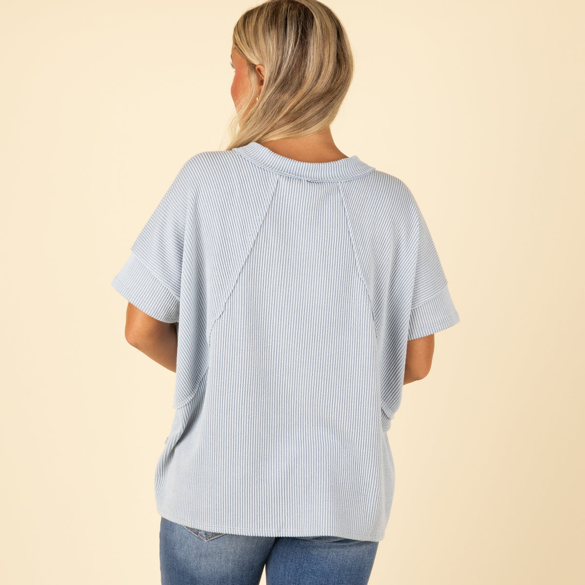 Woman wearing a light blue ribbed top on a beige background
