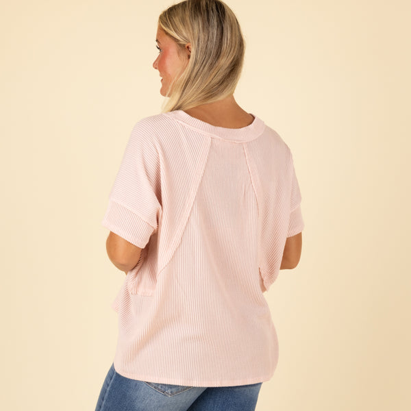 Woman wearing a light pink ribbed top on a beige background