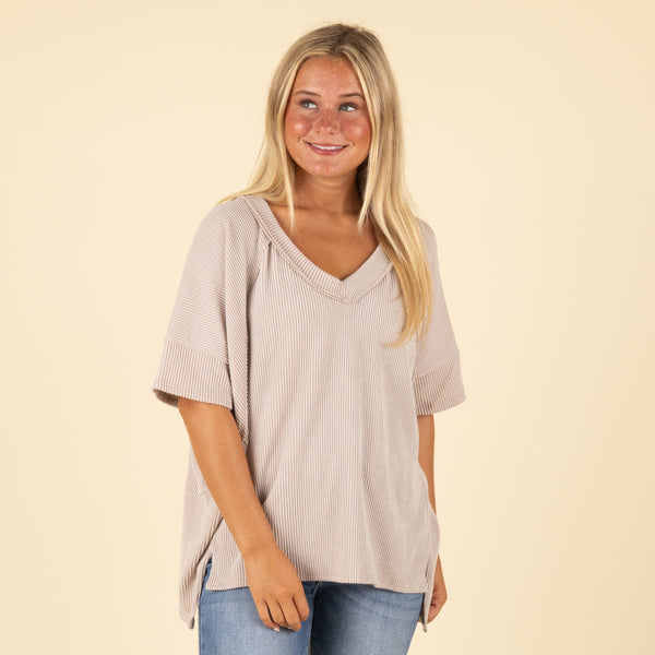 Woman wearing a beige ribbed top and blue jeans on a beige background