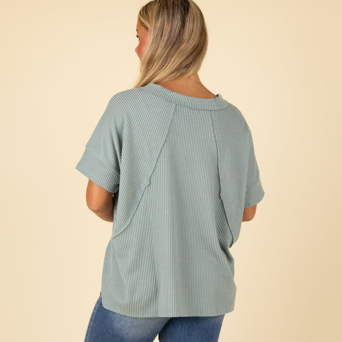 Woman wearing a light green ribbed top with a beige background