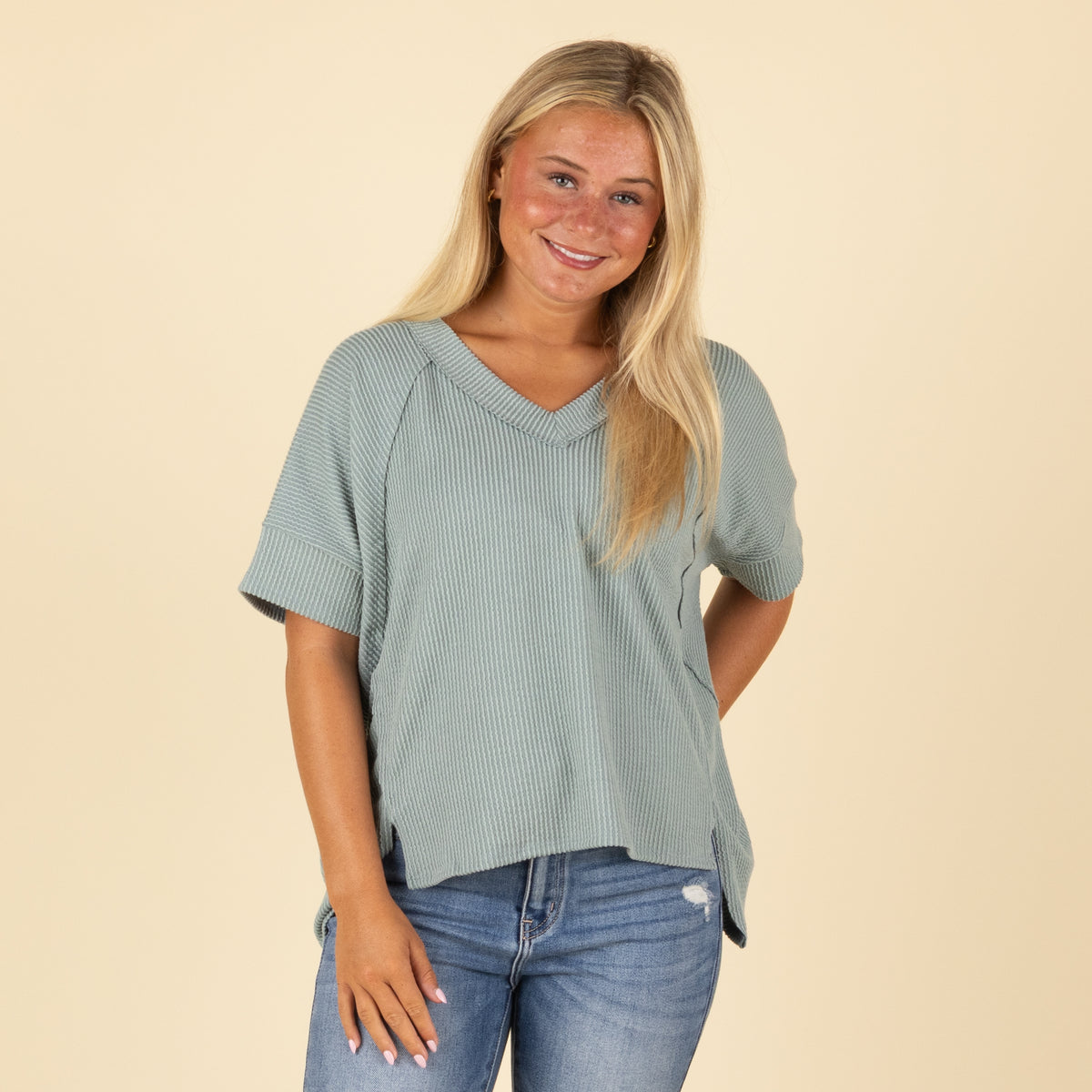 Woman wearing a green ribbed top and blue jeans on a beige background