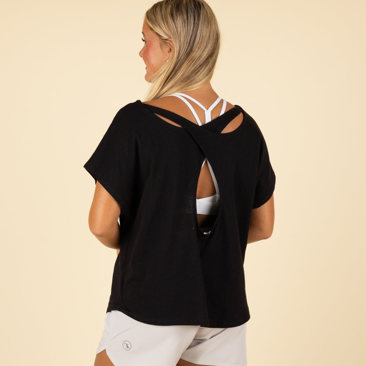 Woman wearing a black open-back top and white shorts on a beige background