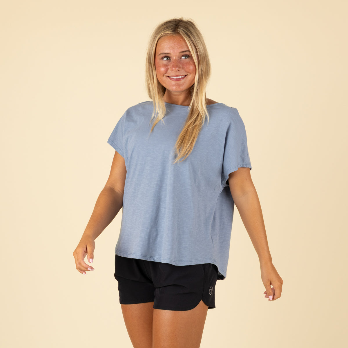 Woman wearing a light blue t-shirt and black shorts on a beige background