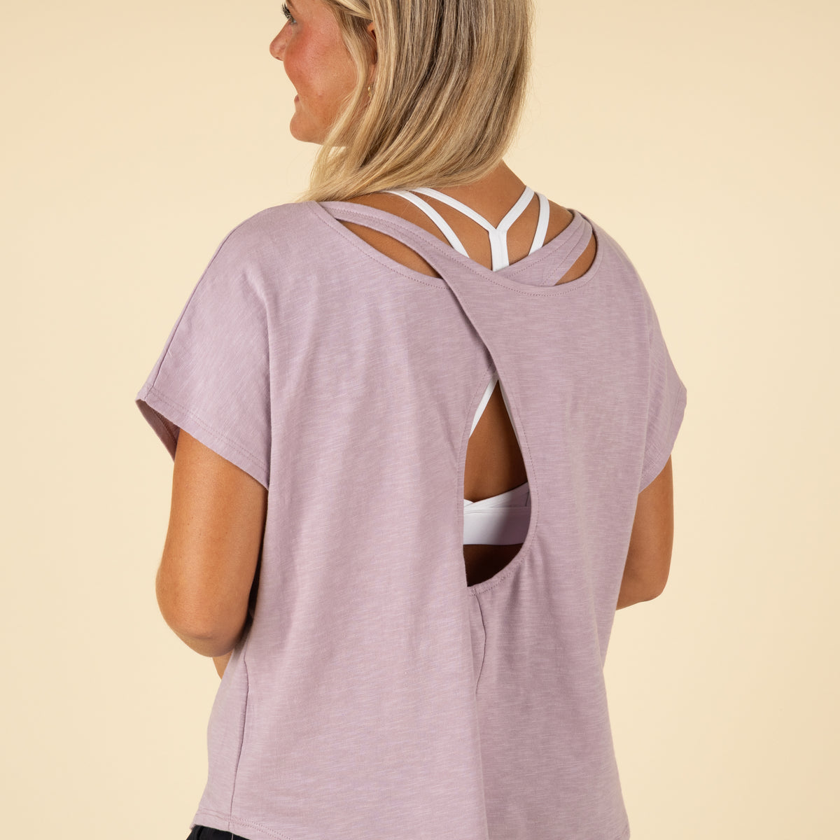Woman wearing a light purple t-shirt with cut-out design on a beige background