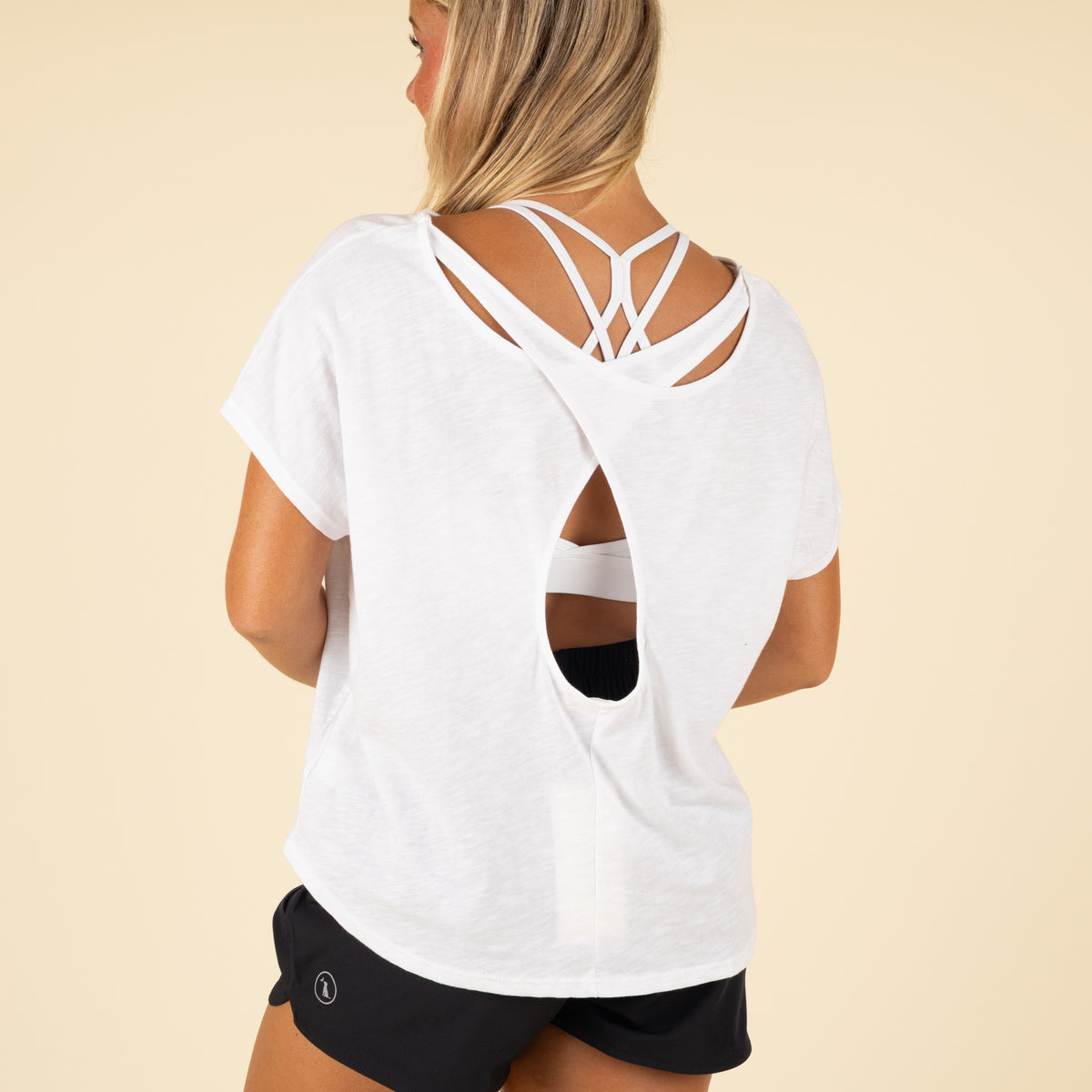Woman wearing a white t-shirt with a unique back design on a beige background