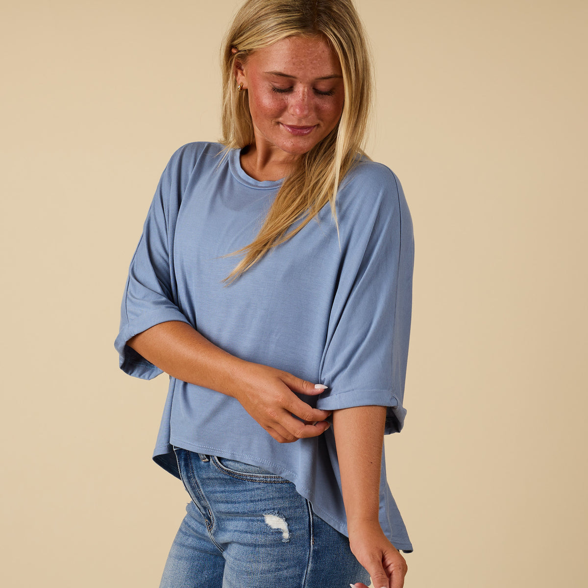 Model wearing hi lo denim blue short sleeve top with relaxed fit, shown from front adjusting rolled sleeve.