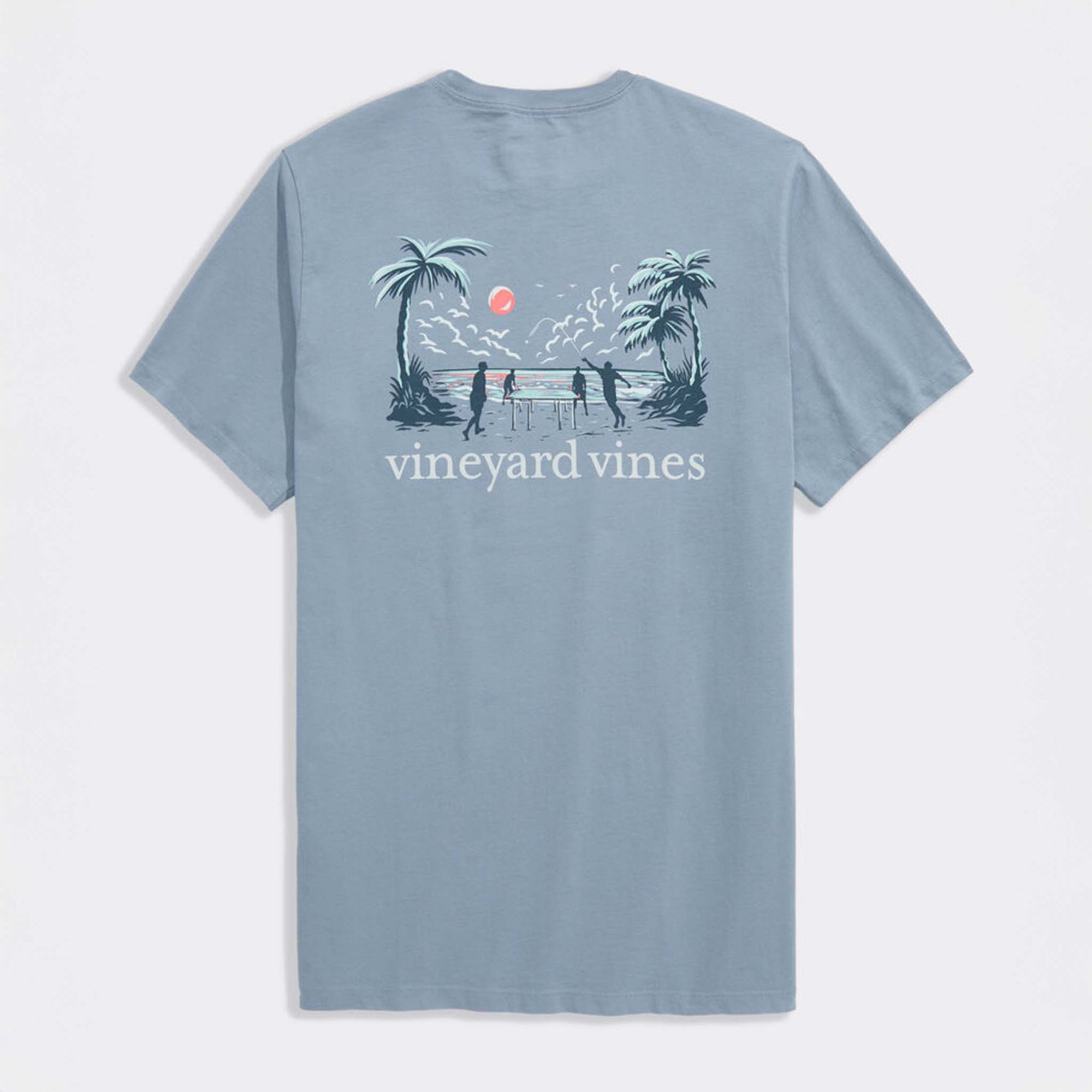 Back view of light blue Vineyard Vines t-shirt featuring beach scene graphic with palm trees, ocean sunset, and players around a table.